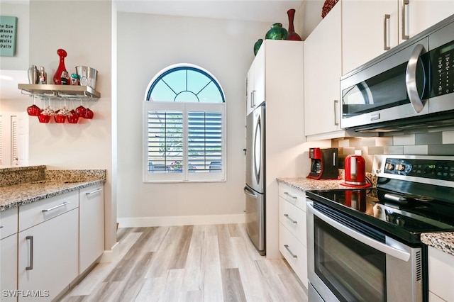 kitchen featuring white cabinetry, tasteful backsplash, light wood-type flooring, stainless steel appliances, and light stone countertops