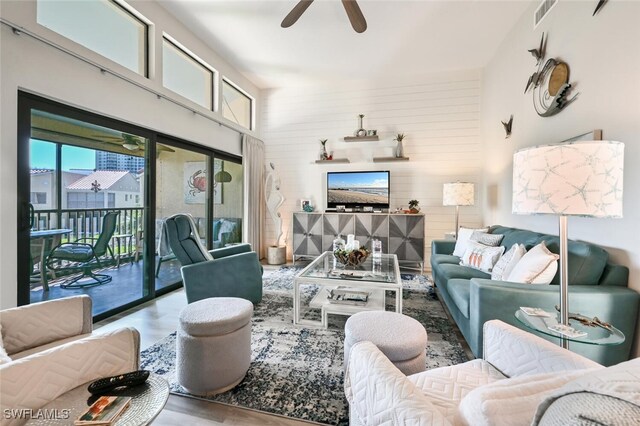 living room with ceiling fan, a towering ceiling, and wood walls