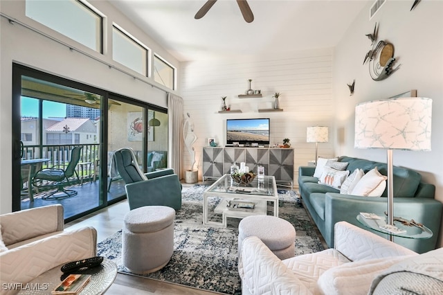 living room with a towering ceiling, wooden walls, and ceiling fan