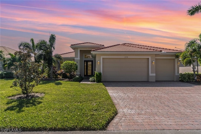 mediterranean / spanish-style house with stucco siding, an attached garage, a tiled roof, and decorative driveway