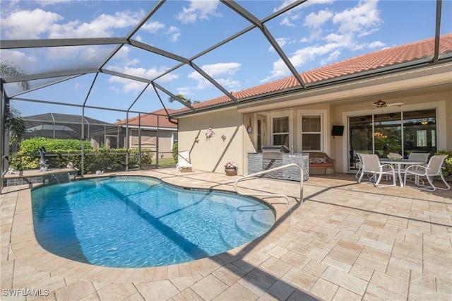 view of pool with a patio, glass enclosure, pool water feature, and ceiling fan