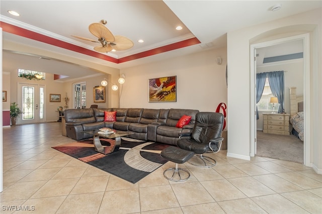 living room featuring ceiling fan, a tray ceiling, ornamental molding, and light tile patterned floors