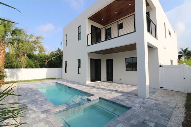 rear view of house featuring a patio, a balcony, and a swimming pool with hot tub