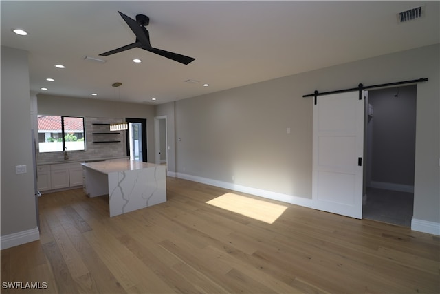 kitchen featuring light wood-type flooring, ceiling fan, a center island, a barn door, and white cabinetry