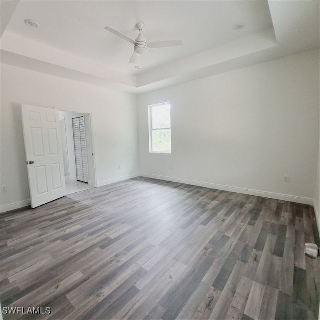 empty room featuring ceiling fan, a tray ceiling, and dark hardwood / wood-style flooring