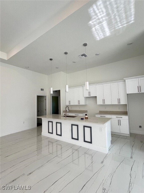 kitchen with sink, a kitchen island with sink, pendant lighting, and white cabinets