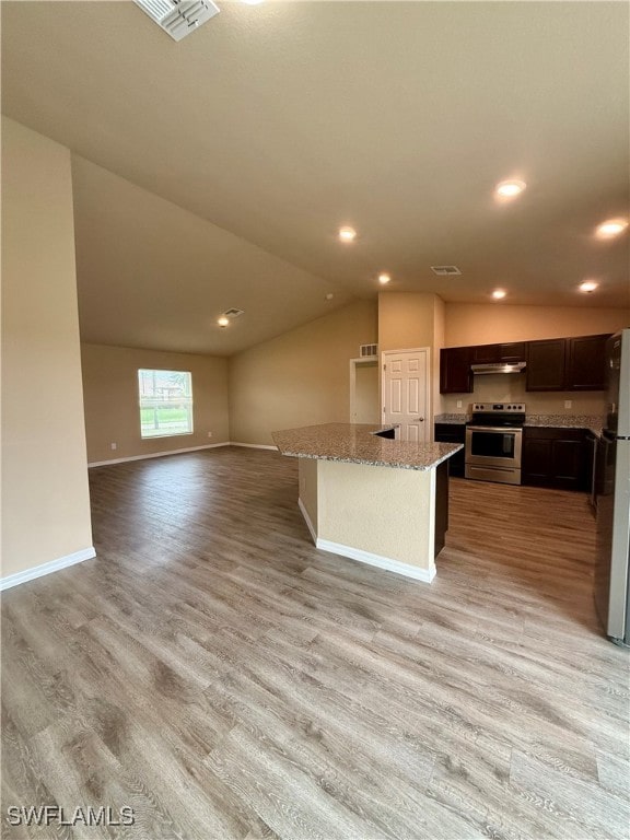 kitchen with a center island, lofted ceiling, light wood-type flooring, light stone counters, and stainless steel appliances