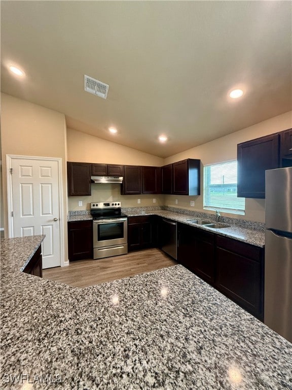 kitchen with sink, vaulted ceiling, dark brown cabinets, appliances with stainless steel finishes, and light wood-type flooring