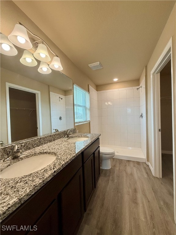 bathroom with a tile shower, vanity, wood-type flooring, and toilet