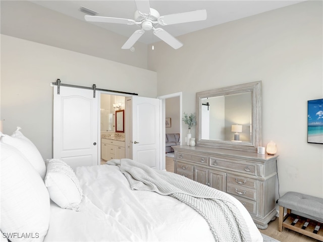 bedroom featuring a high ceiling, a barn door, ensuite bathroom, light hardwood / wood-style floors, and ceiling fan