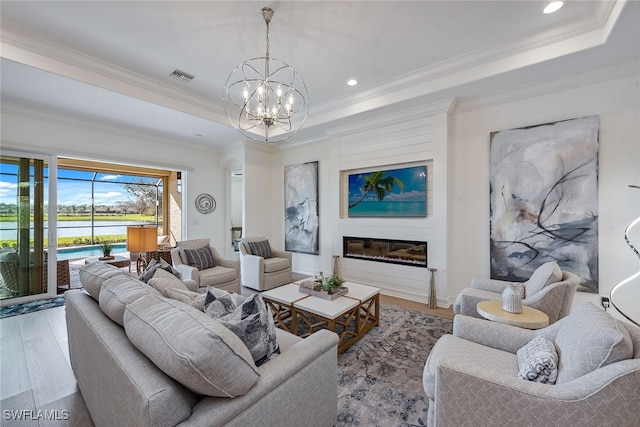 living room with an inviting chandelier, crown molding, a tray ceiling, and light hardwood / wood-style floors