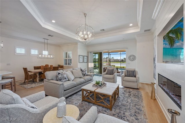 living room featuring crown molding, a tray ceiling, light wood-type flooring, and an inviting chandelier