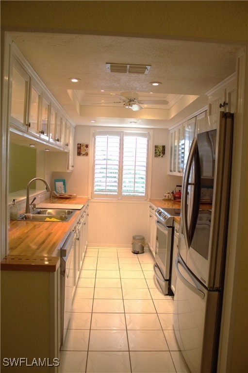 kitchen with a raised ceiling, white cabinetry, ornamental molding, sink, and stainless steel appliances