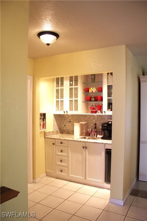 bar featuring decorative backsplash, white cabinets, a textured ceiling, light stone countertops, and sink