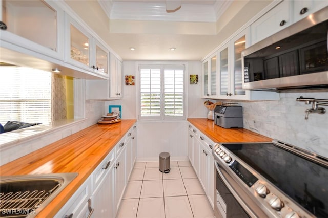 kitchen featuring light tile patterned flooring, tasteful backsplash, white cabinetry, butcher block counters, and stainless steel appliances