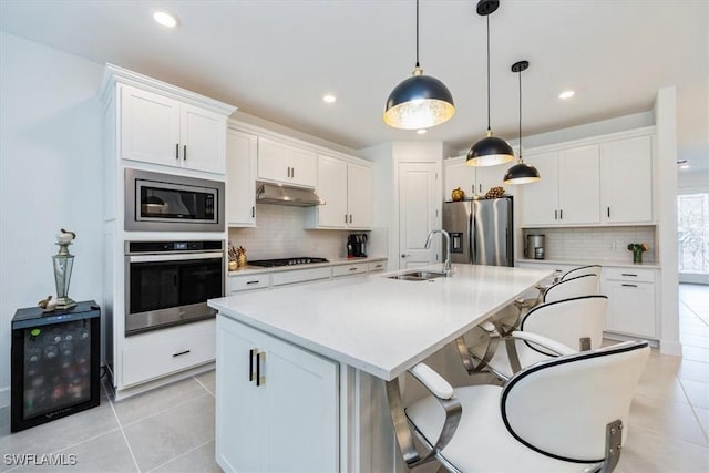 kitchen with appliances with stainless steel finishes, decorative light fixtures, white cabinetry, sink, and a center island with sink