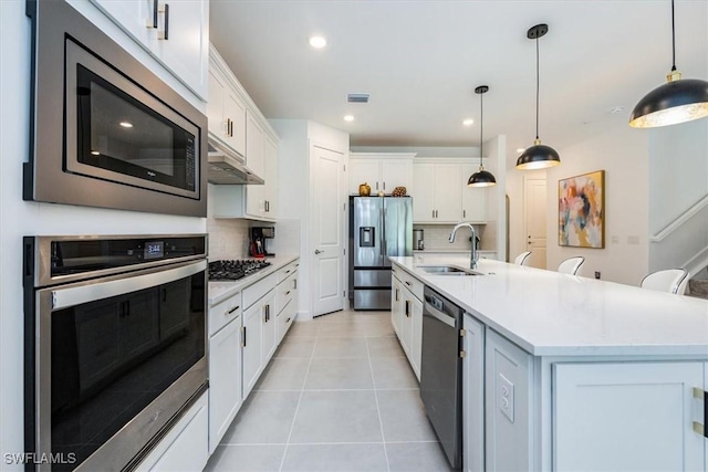 kitchen featuring sink, appliances with stainless steel finishes, pendant lighting, a kitchen island with sink, and white cabinets