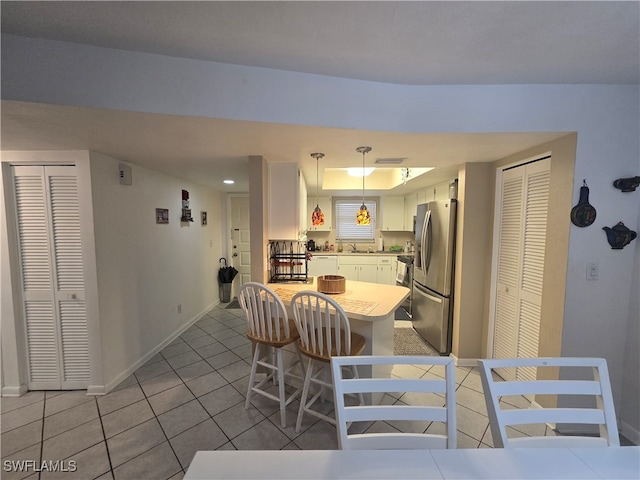 kitchen featuring stainless steel fridge, light tile patterned flooring, pendant lighting, white cabinetry, and a breakfast bar area