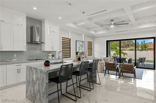 kitchen with wall chimney exhaust hood, sink, white cabinetry, and a center island with sink