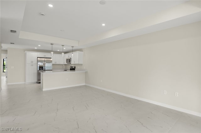 kitchen with hanging light fixtures, stainless steel appliances, a tray ceiling, kitchen peninsula, and white cabinetry