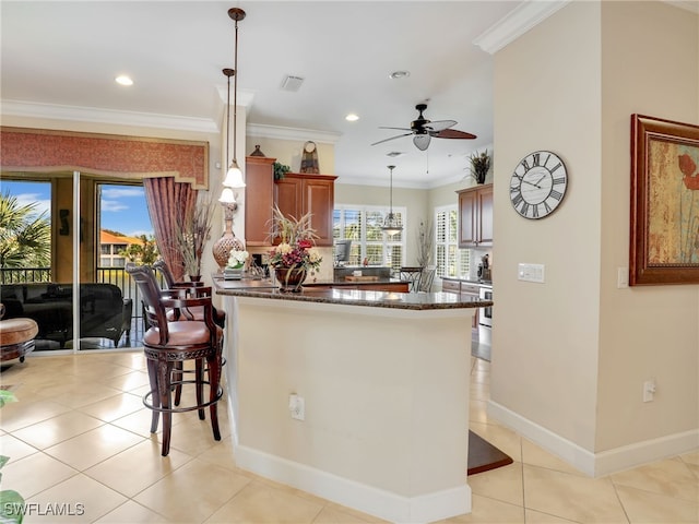 kitchen featuring ceiling fan, pendant lighting, a kitchen breakfast bar, ornamental molding, and light tile patterned floors