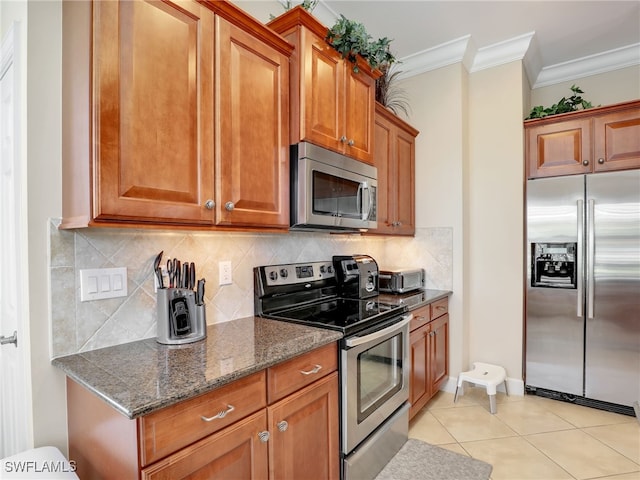 kitchen with decorative backsplash, stainless steel appliances, light tile patterned flooring, dark stone counters, and ornamental molding