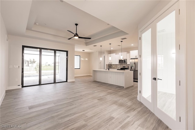 unfurnished living room featuring a raised ceiling, ceiling fan, sink, and light hardwood / wood-style flooring