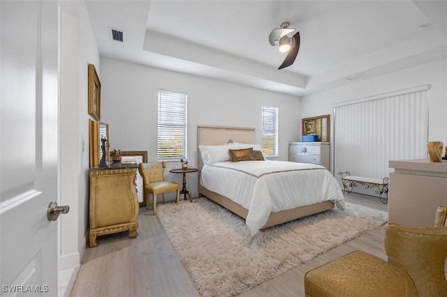 bedroom featuring a tray ceiling, visible vents, ceiling fan, and light wood finished floors