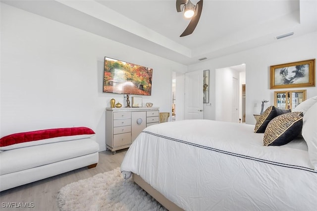 bedroom with ensuite bathroom, a raised ceiling, ceiling fan, and light wood-type flooring