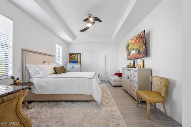 bedroom featuring ceiling fan, a tray ceiling, light wood-type flooring, and baseboards