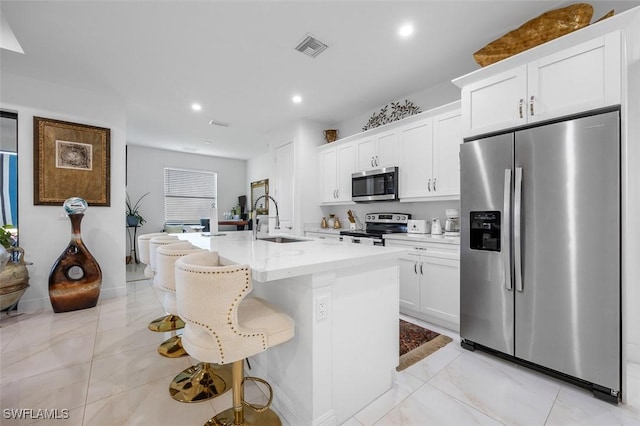 kitchen featuring a sink, visible vents, white cabinetry, appliances with stainless steel finishes, and a center island with sink