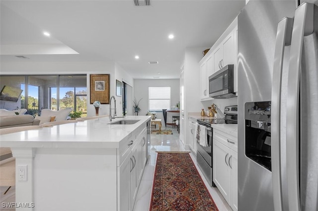 kitchen featuring sink, a tray ceiling, an island with sink, stainless steel appliances, and white cabinets