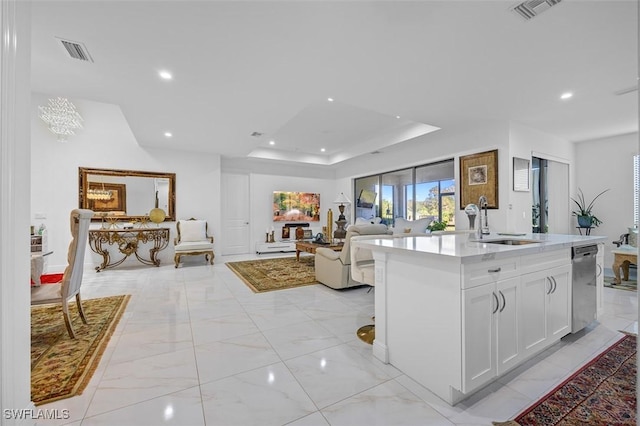 kitchen featuring sink, stainless steel dishwasher, a raised ceiling, an island with sink, and white cabinets