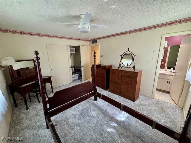 carpeted bedroom with a closet, a textured ceiling, ensuite bathroom, and ceiling fan