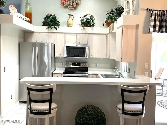 kitchen featuring a kitchen bar, light brown cabinetry, kitchen peninsula, stainless steel appliances, and sink