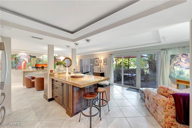 kitchen with a raised ceiling, light tile patterned flooring, butcher block counters, and a breakfast bar area