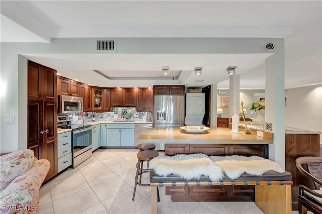 kitchen featuring sink, light tile patterned floors, stainless steel appliances, a tray ceiling, and decorative backsplash