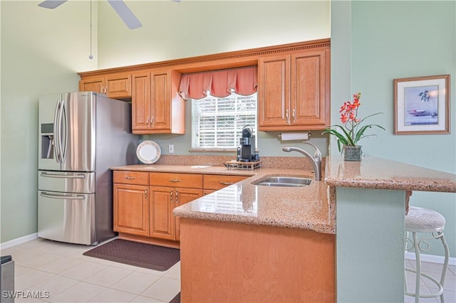 kitchen featuring a breakfast bar, sink, stainless steel fridge, light stone countertops, and kitchen peninsula