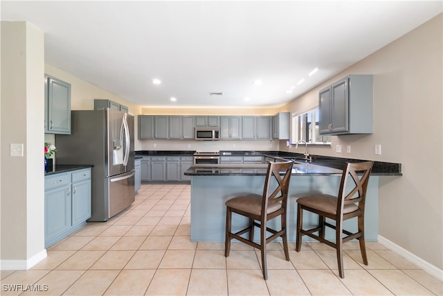 kitchen with appliances with stainless steel finishes, light tile patterned floors, a kitchen breakfast bar, sink, and kitchen peninsula