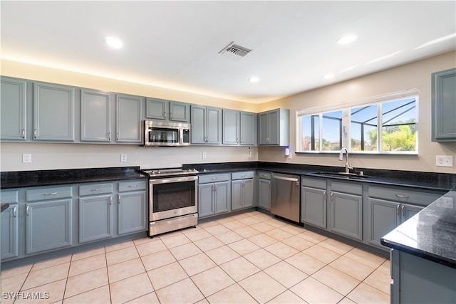 kitchen with light tile patterned floors, gray cabinetry, sink, dark stone countertops, and stainless steel appliances