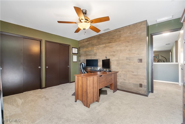 office featuring ceiling fan, light colored carpet, and wood walls