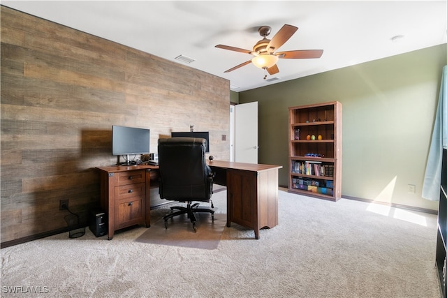 carpeted office with ceiling fan and wood walls