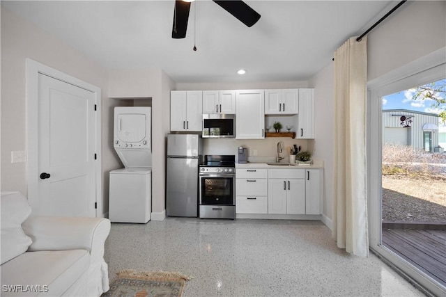 kitchen featuring stacked washer and clothes dryer, sink, ceiling fan, stainless steel appliances, and white cabinets