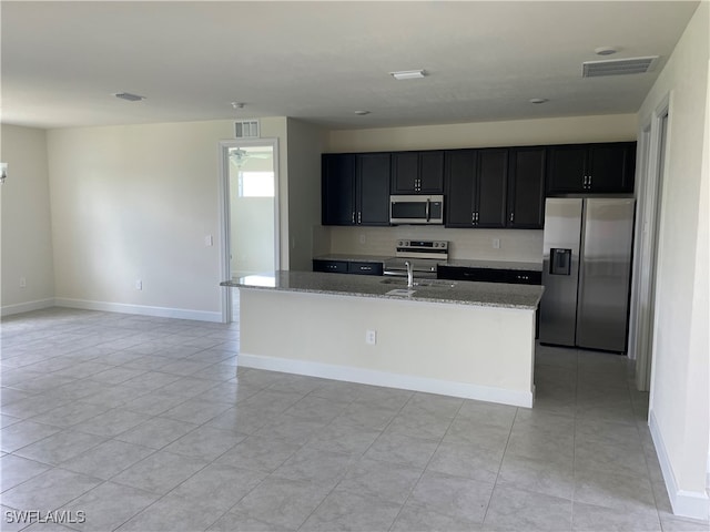 kitchen featuring light stone countertops, sink, light tile patterned flooring, stainless steel appliances, and a center island with sink