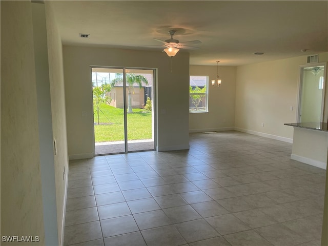 tiled empty room with ceiling fan with notable chandelier