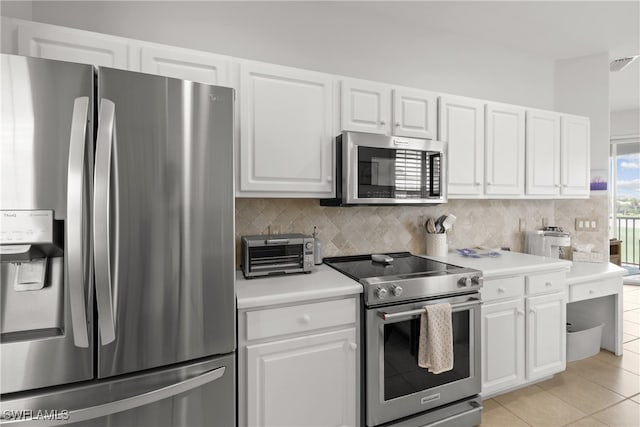 kitchen with appliances with stainless steel finishes, decorative backsplash, white cabinets, and light tile patterned floors