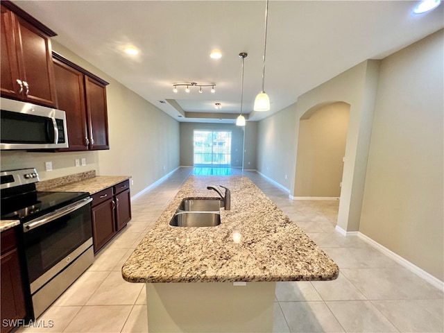 kitchen with light stone countertops, appliances with stainless steel finishes, a kitchen island with sink, sink, and hanging light fixtures