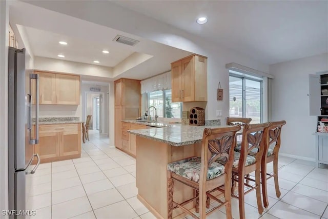 kitchen with light brown cabinetry, a breakfast bar area, and stainless steel fridge