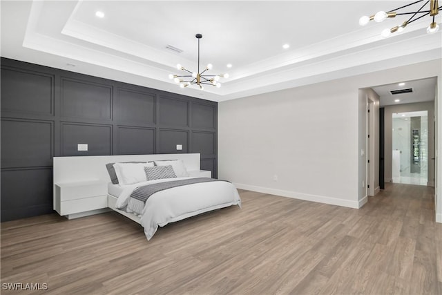 bedroom featuring light hardwood / wood-style floors, a raised ceiling, and an inviting chandelier