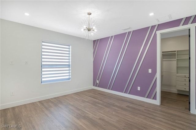 unfurnished bedroom with a walk in closet, a chandelier, a closet, and wood-type flooring